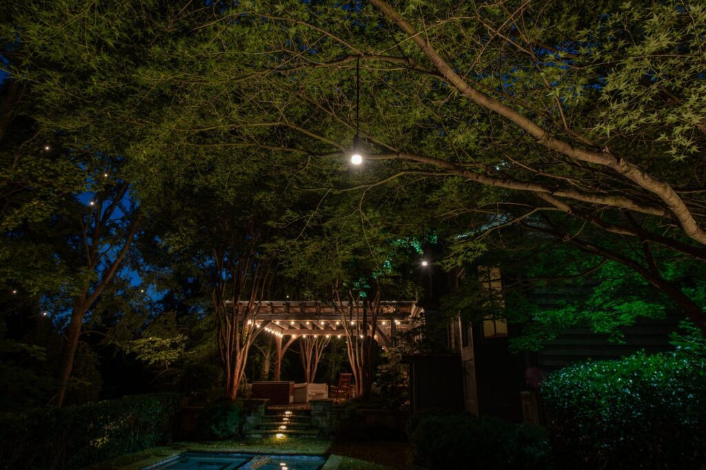 Backyard pergola with string lights, tree uplighting and step lights at night by NightVision Outdoor Lighting